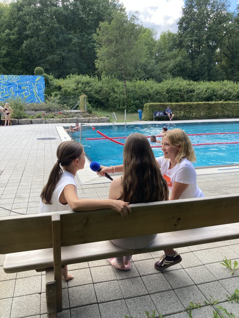 Luisa interviewt junge Badegäste im Freibad Rieden zu ihren Musikwünschen